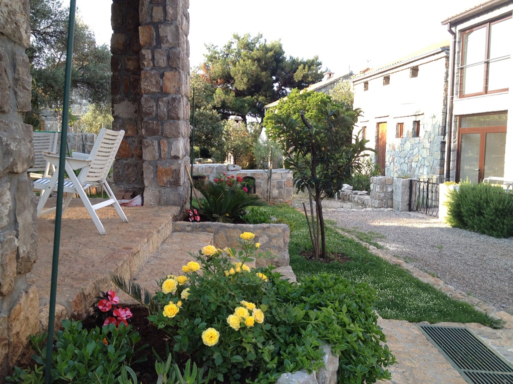 Terrasse einer Steinvilla in Luštica, Montenegro, mit Garten, blühenden Rosen und Blick auf einen gemütlichen Innenhof.