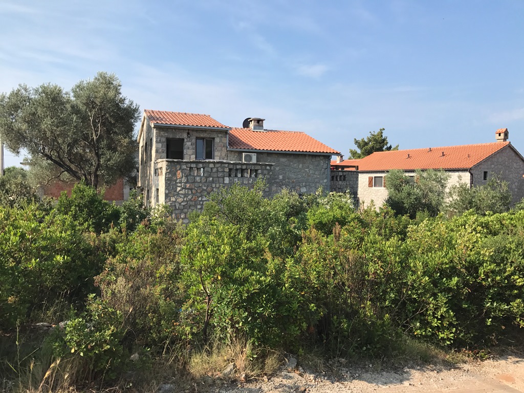 Steinvilla mit Ziegeldach inmitten von Grün, Luštica, Montenegro. Blick auf die Fassade des Hauses im mediterranen Stil.