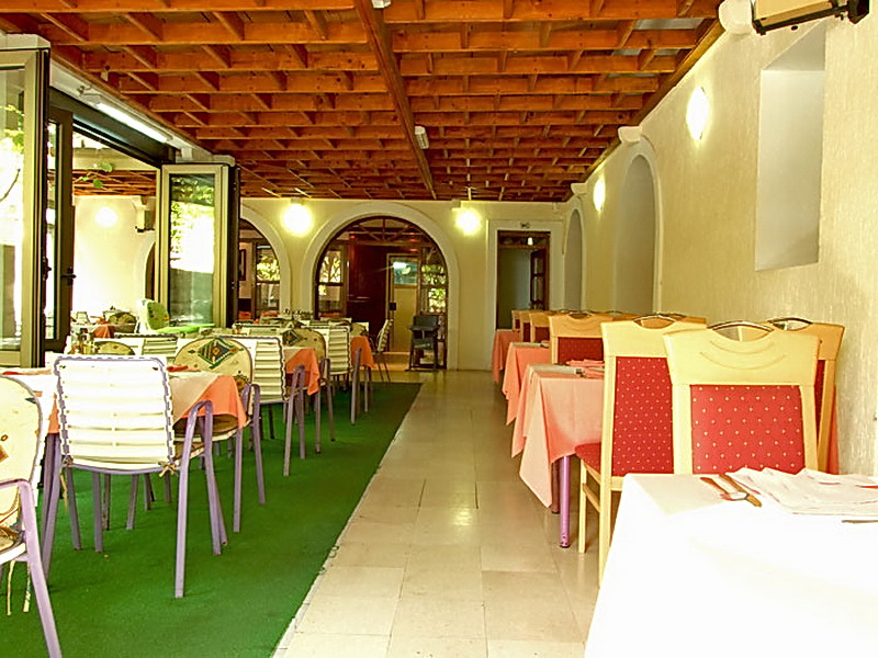 Innenraum des Hotelrestaurants in Petrovac, Montenegro: überdachte Terrasse mit Holzdecke, Tischen und Stühlen für Gäste.