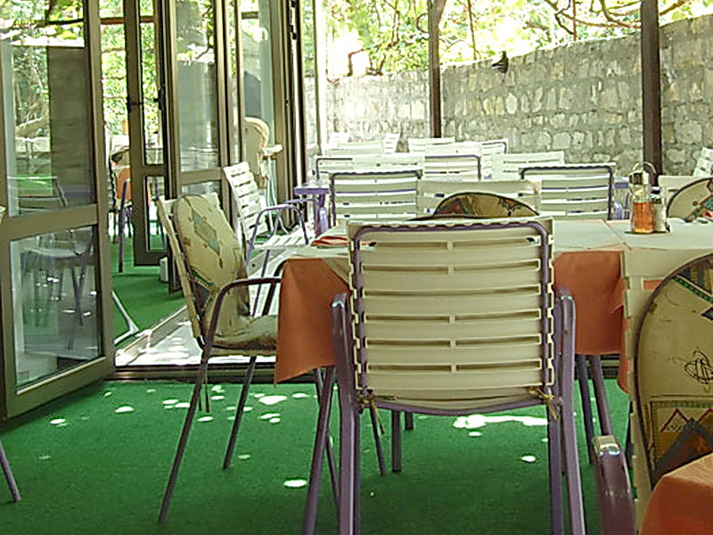 Sommerterrasse des Hotels in Petrovac, Montenegro: Tische mit orangefarbenen Tischdecken und Plastikstühle im Freien.