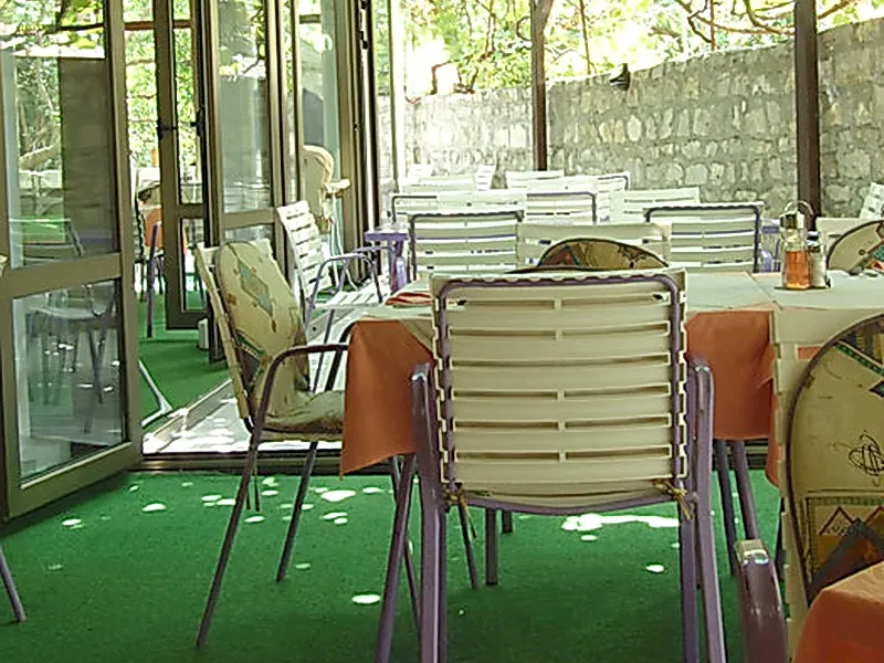 Sommerterrasse des Hotels in Petrovac, Montenegro: Tische mit orangefarbenen Tischdecken und Plastikstühle im Freien.