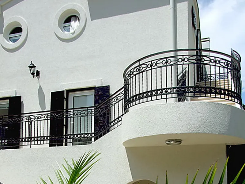 Fassade des Hotels in Petrovac, Montenegro: weiße Wände, runde Fenster und schmiedeeiserne Geländer auf der Terrasse des Gebäudes.