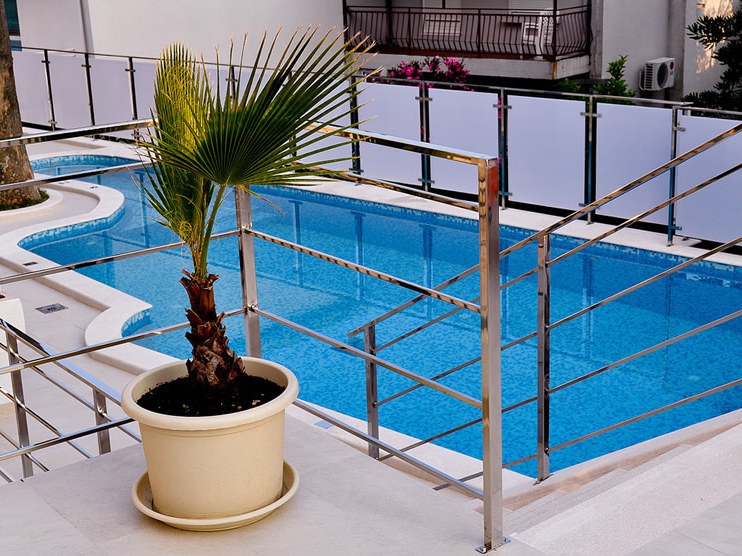 Offener Pool mit blauem Wasser und Palme im Topf auf der Terrasse des Hotels in Petrovac, Montenegro.