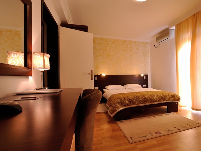 Gemütliches Schlafzimmer mit Doppelbett und Schreibtisch im Hotel Petrovac, Montenegro. Helles Interieur mit Dekor.