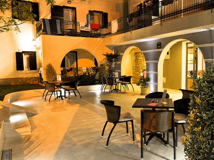 Abendterrasse des Hotels in Petrovac, Montenegro: gemütlicher Ruhebereich mit Rattanmöbeln und bogenförmigen Gebäudedurchgängen.