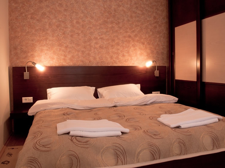 Gemütliches Schlafzimmer mit Doppelbett im Hotel Petrovac, Montenegro: dunkle Möbel, Wandleuchten und Dekor.