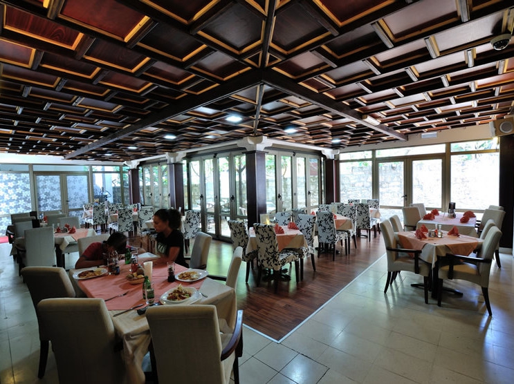 Innenraum des Hotelrestaurants in Petrovac, Montenegro: Kassettendecke aus Holz, Panoramafenster und weiche Stühle.
