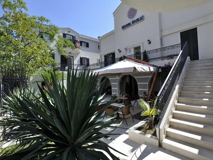 Fassade des Hotels Durc in Petrovac, Montenegro: gemütliche Terrasse mit Tischen, Außentreppe und grüne Anlage.
