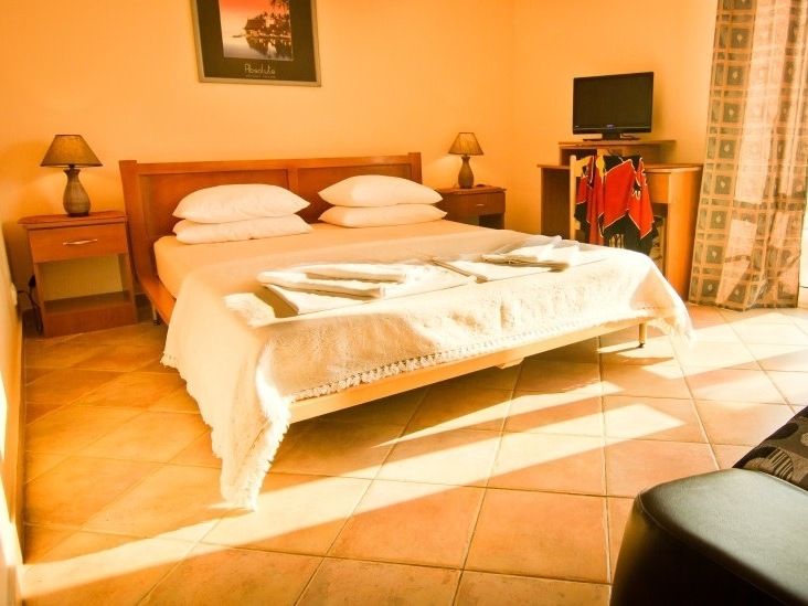 Gemütliches Schlafzimmer mit Doppelbett im Hotel in Sutomore, Montenegro: Fliesenboden, Nachttische und TV-Bereich.