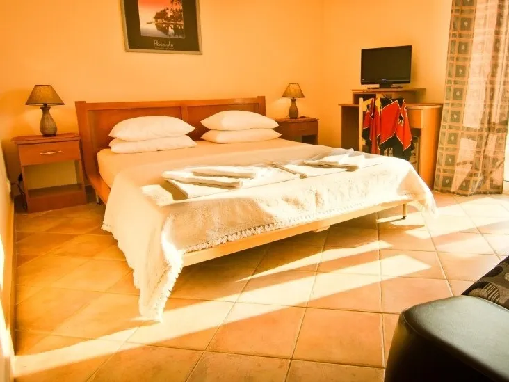Gemütliches Schlafzimmer mit Doppelbett im Hotel in Sutomore, Montenegro: Fliesenboden, Nachttische und TV-Bereich.