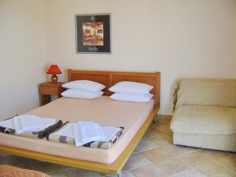 Schlafzimmer im Hotel in Sutomore, Montenegro: Doppelbett, Sessel, Nachttisch und Fliesenboden.