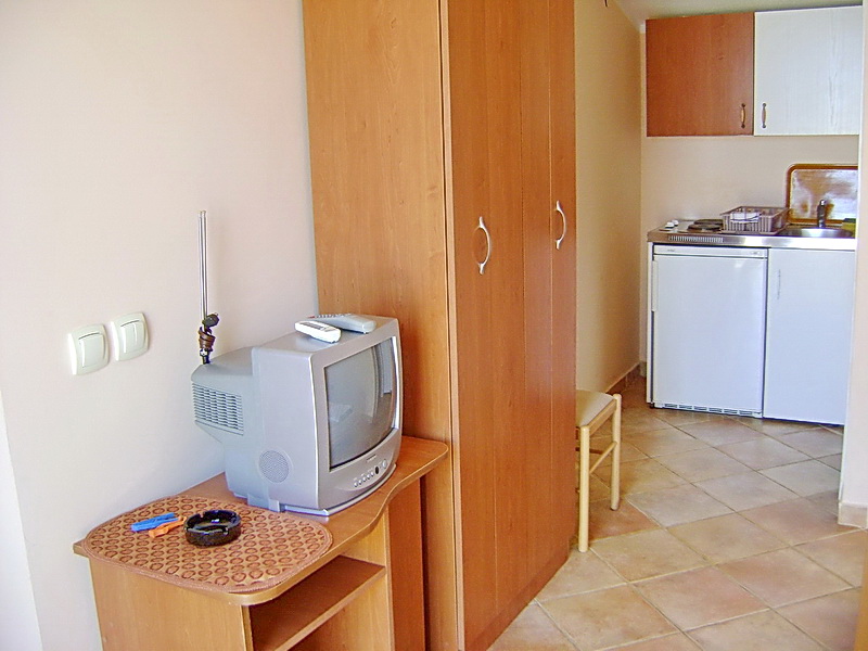 Innenraum eines Hotelzimmers in Sutomore, Montenegro: kompakte Küche, Holzschrank und Fernseher auf einem Sideboard.