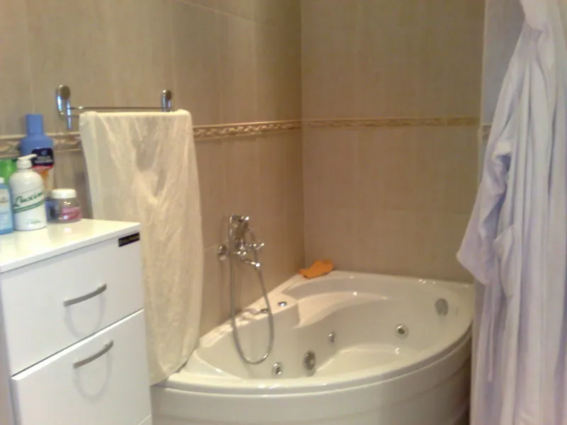 Badezimmer mit Eckbadewanne, weißem Kommodenschrank und Handtuch an der Wand.