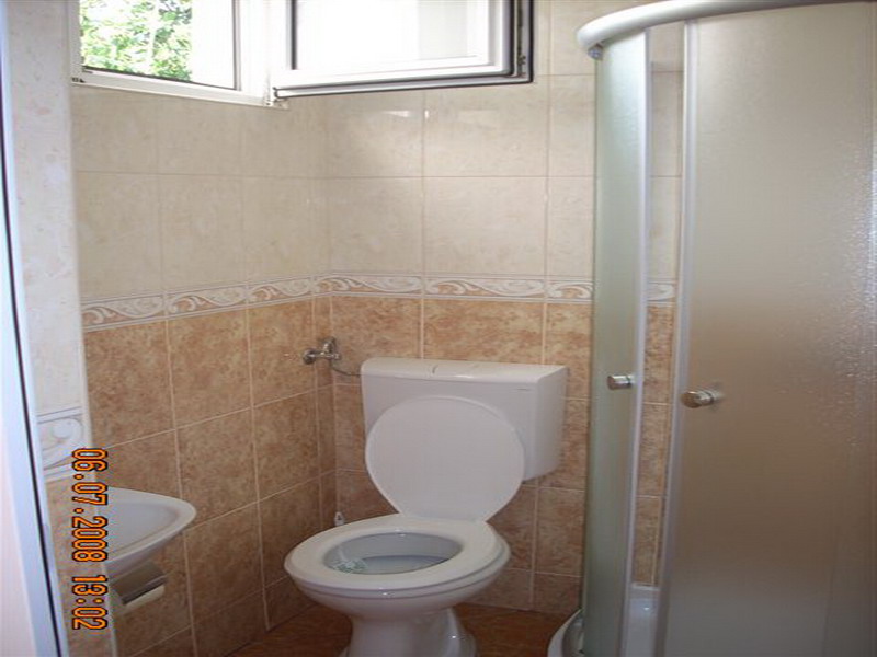 Kupatilo u kući u Sutomoru, Crna Gora: svetle pločice, tuš kabina, WC šolja i prozor za ventilaciju.