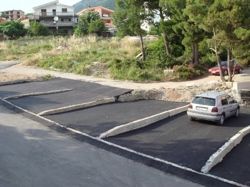 Ansicht eines Parkplatzes von oben mit Autos und Häusern im Hintergrund.