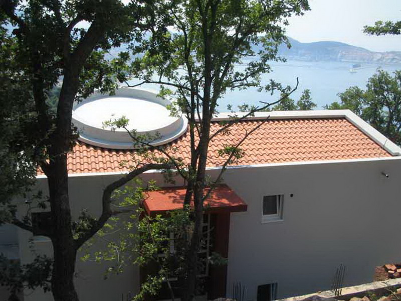 Modernes Haus mit Ziegeldach und Meerblick in Šušanj, Montenegro, umgeben von Grün und Bäumen.