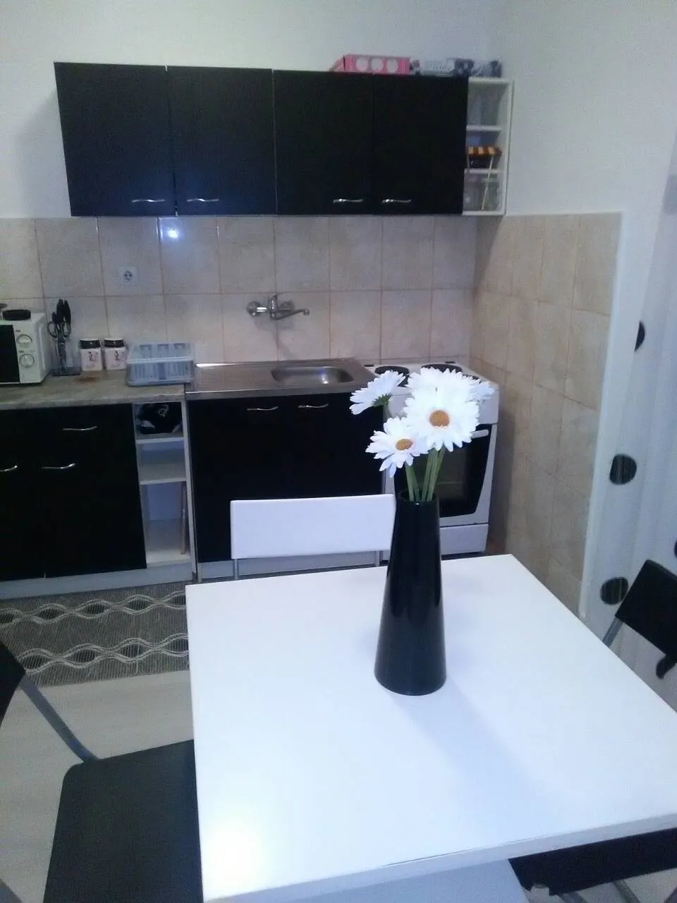 Eine kompakte Küche mit dunklen Schränken, einem weißen Esstisch und einer Blumenvase im Vordergrund.
