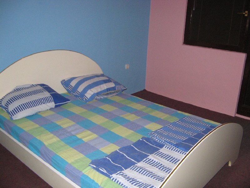 Schlafzimmer mit Doppelbett im Haus, Shushan, Montenegro: helle Wände, karierte Bettwäsche und dunkler Boden.