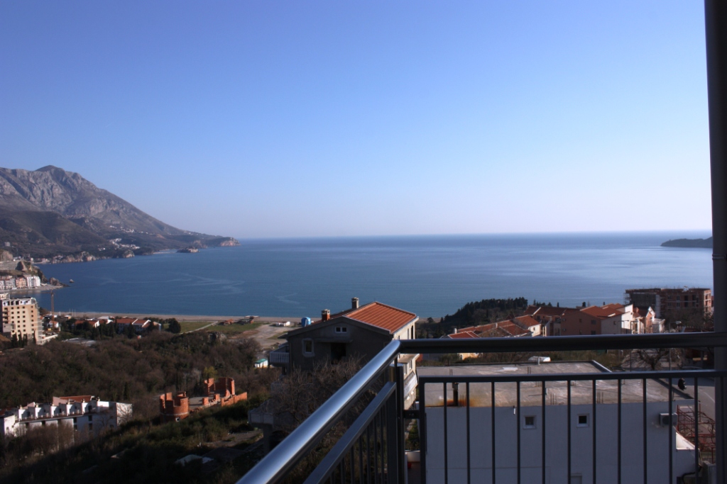 Becici, Karadağ’daki dairenin balkonundan deniz ve dağların panoramik manzarası, metal teras korkuluğu ile.