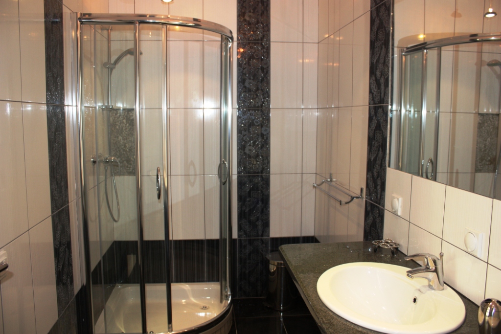 Karadağ, Bečići’deki dairede banyo: duş kabini, tezgahlı lavabo ve siyah-beyaz tonlarda fayanslar.