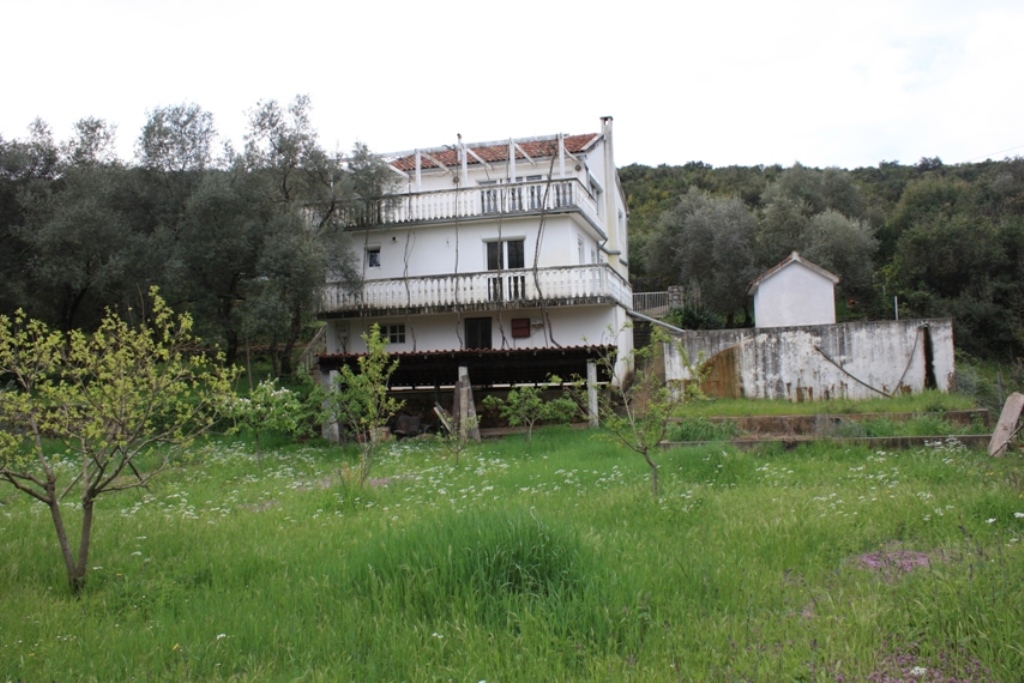Dreistöckiges Haus mit Terrassen und Garten im Ort Bigovo, Montenegro, Blick auf die Fassade und das angrenzende Grundstück mit Bäumen.