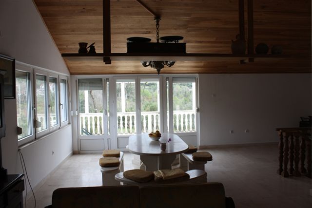 Wohnzimmer mit Holzdecke und Essbereich in einem Haus in Bigovo, Montenegro, mit Zugang zur Terrasse und Blick auf den Garten.
