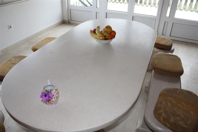 Essbereich mit Steintisch und Bänken im Wohnzimmer eines Hauses in Bigovo, Montenegro. Helles Interieur mit Zugang zur Terrasse.