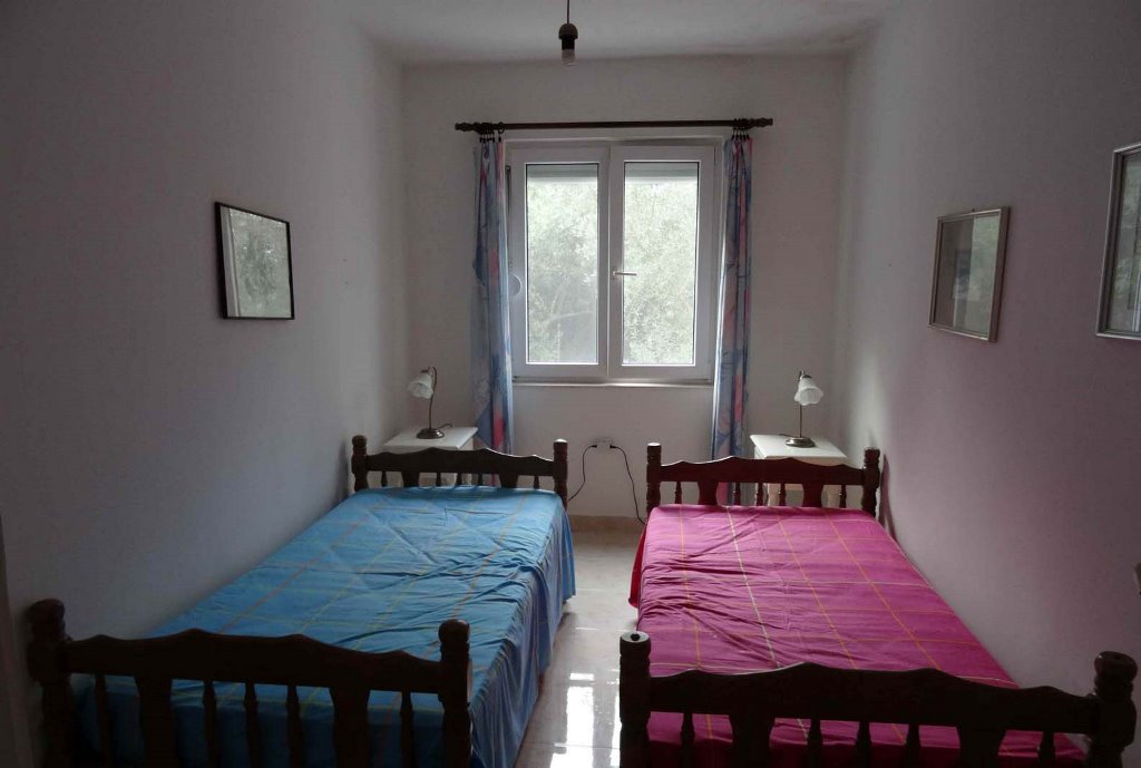 Schlafzimmer mit zwei Betten in einem Haus in Bigovo, Montenegro: heller Raum mit Fenster und Möbeln aus dunklem Holz.