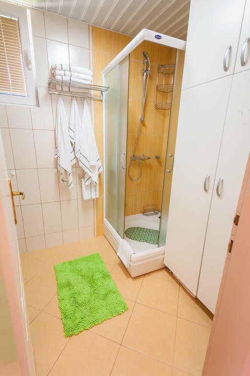 Badezimmer mit Duschkabine und weißem Schrank im Haus, Krumovica, Montenegro. Helle Fliesen und ein leuchtend grüner Teppich.