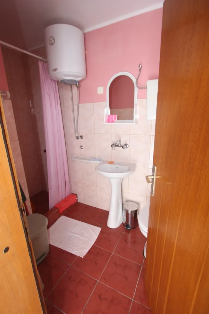 Badezimmer in einem Haus in Utjeha, Montenegro: Dusche mit rosa Vorhang, Waschbecken, Boiler und Fliesenverkleidung.