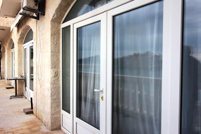 Terrasse mit Steinverkleidung und Panoramafenstern in einer Wohnung in Sveti Stefan, Montenegro, mit Meer- und Inselblick.