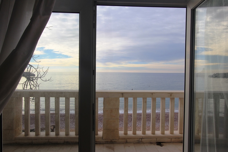 Meer- und Strandblick vom Balkon der Wohnung in Sveti Stefan, Montenegro: Steinbrüstung und Panoramafenster.