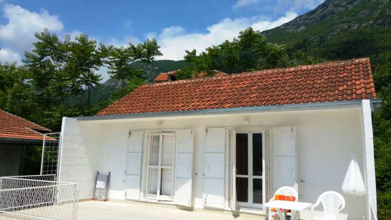 White house with a tiled roof and terrace in Risan, Montenegro: mountain view and facade with white shutters.
