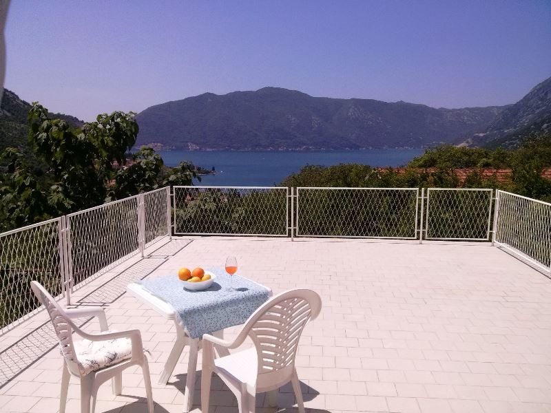 Terrace with a view of the Bay of Kotor, house in Risan, Montenegro: white furniture, tiled flooring, and panoramic views.