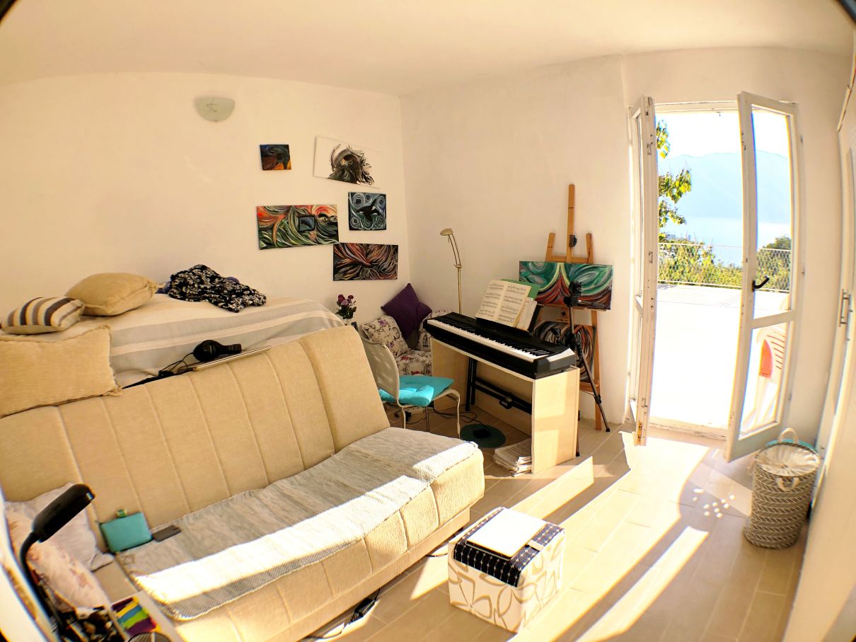 Living room with a sofa, piano, and access to a terrace with sea views in a house in Risan, Montenegro.