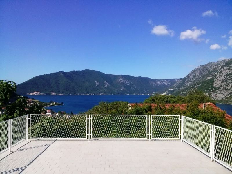 Panoramic view of the Bay of Kotor from the open terrace of a house in Risan, Montenegro, with a white metal railing.