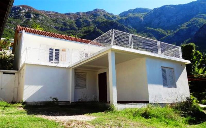 Two-story house with a terrace and mountain views in Risan, Montenegro. White facade, tiled roof, and green grounds.