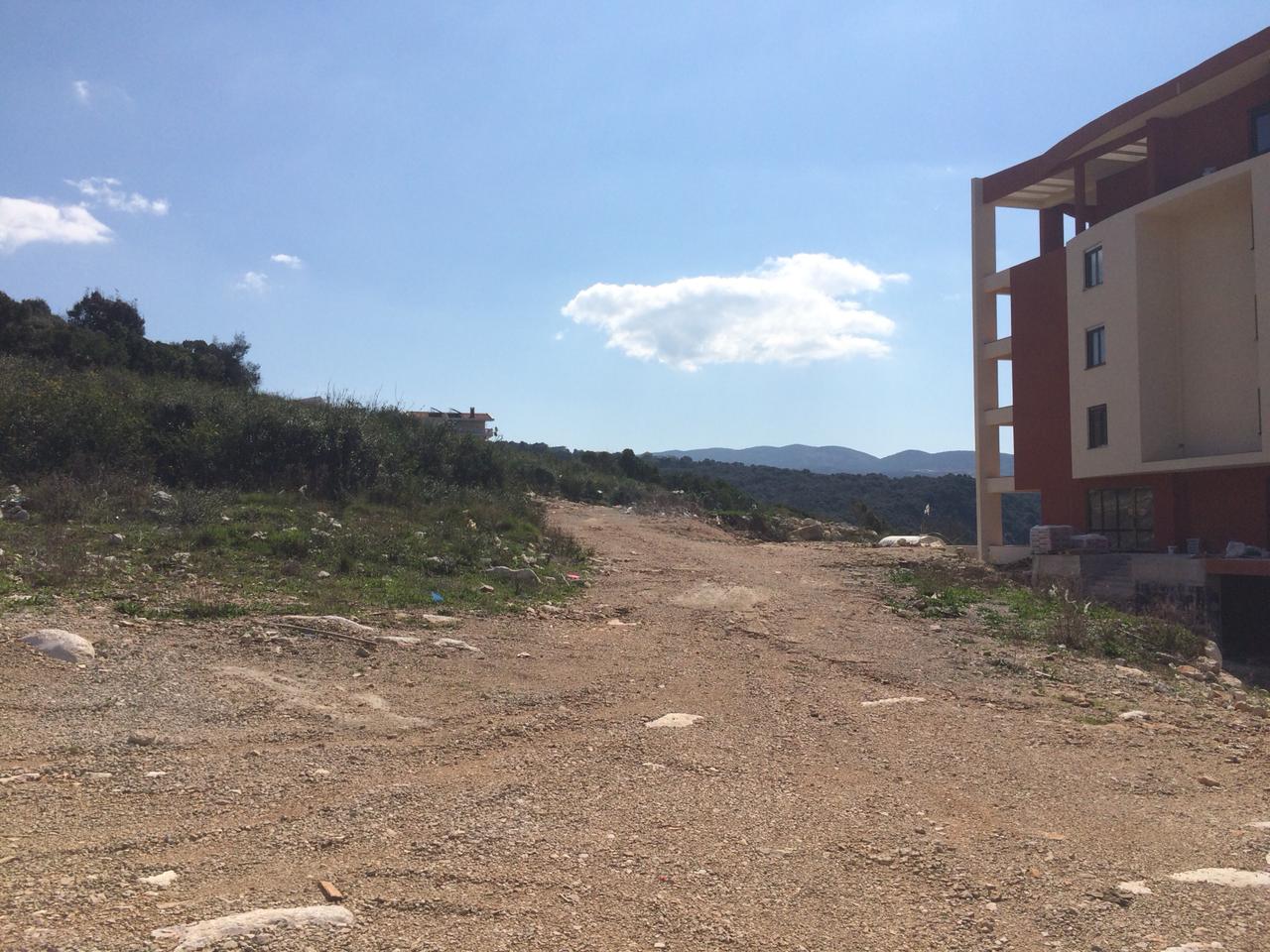 Baugrundstück in Dobri Vody, Montenegro, mit Bergblick und modernem Wohnhaus in der Nähe.