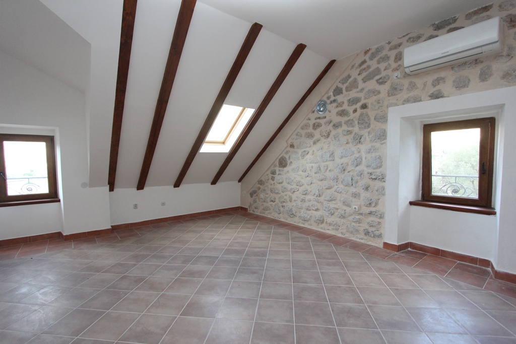 Living room in a villa in Prčanj, Montenegro: attic with a stone wall, wooden beams, and tiled floor.