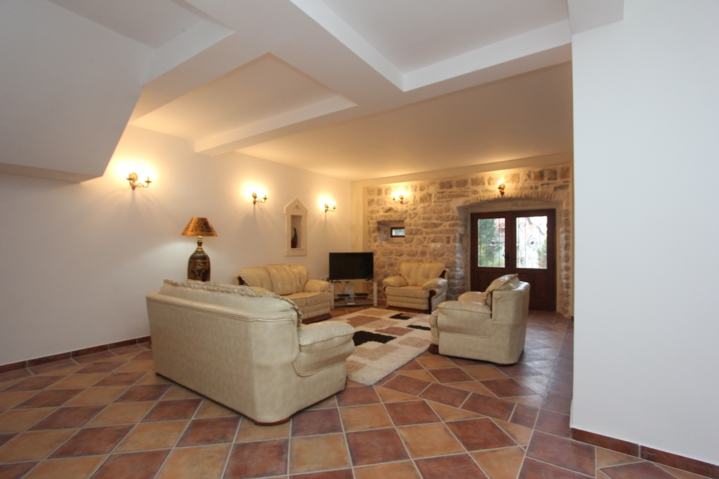 Living room in a villa in Prčanj, Montenegro: light furniture, stone walls, and tiled flooring in the interior.