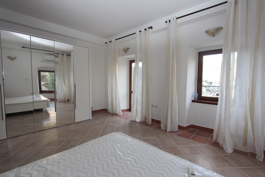 Bright bedroom with a mirrored wardrobe and tiled floor in a villa in Prčanj, Montenegro, sea view from the window.