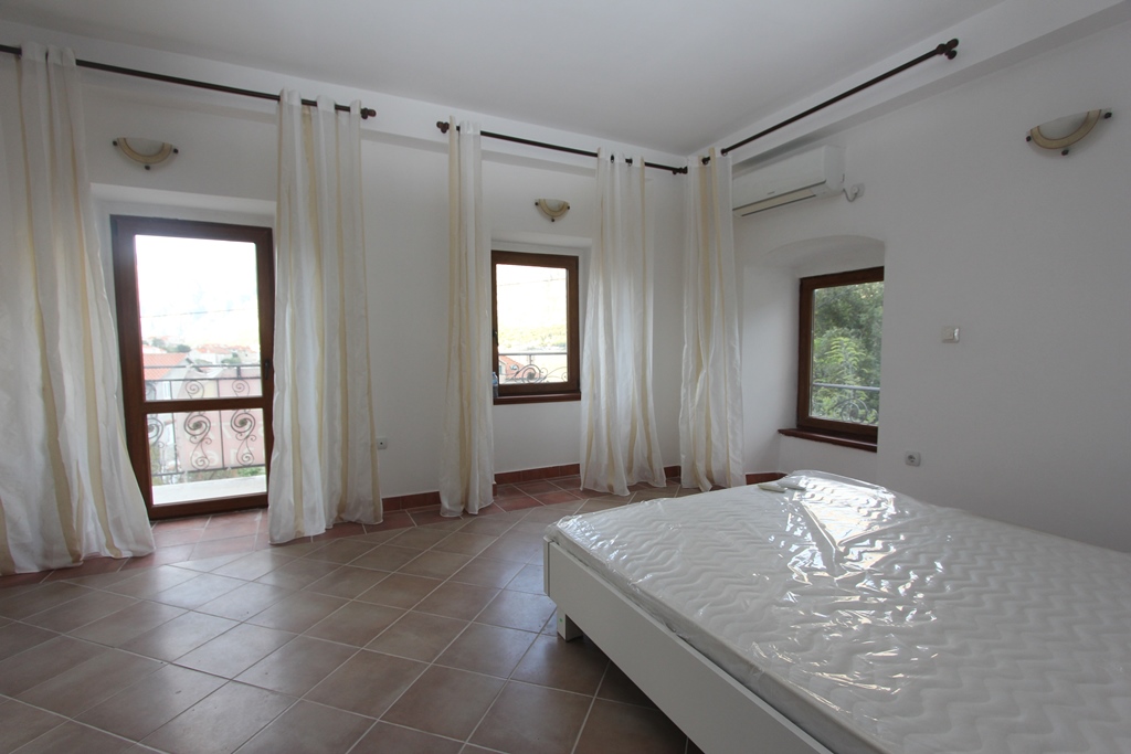 Bright bedroom with a double bed and access to the balcony in a villa in Prčanj, Montenegro, tiled floor and city view.