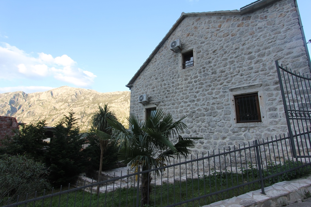 Facade of a stone villa in Prčanj, Montenegro: traditional masonry, air conditioners, mountain view, and palm trees in the courtyard.