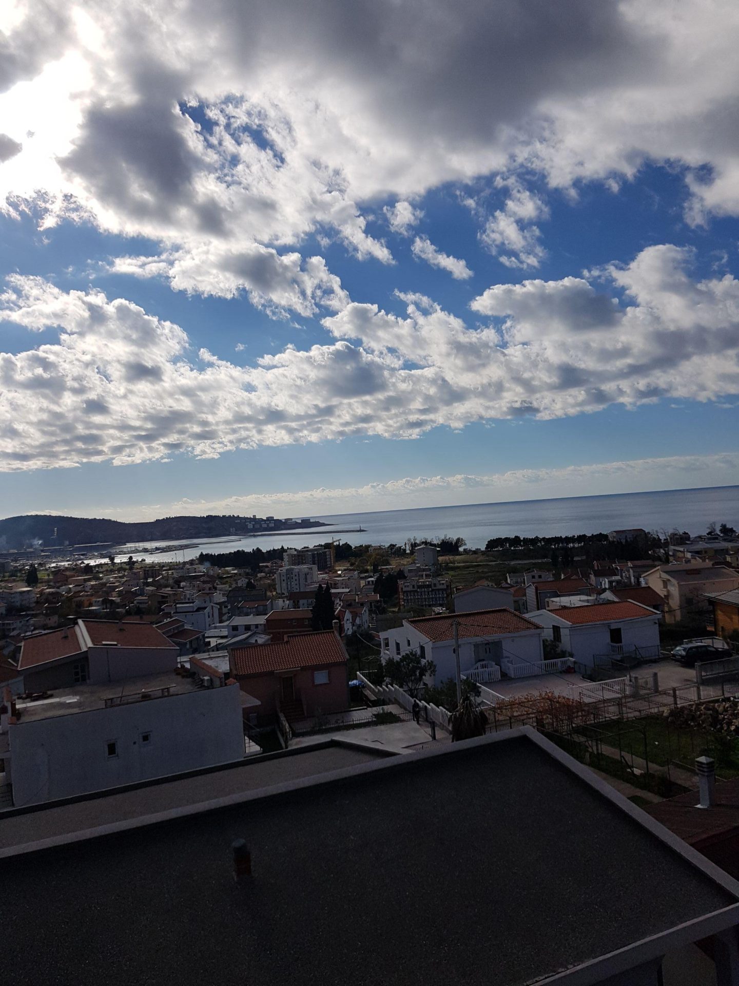 Panoramablick auf das Meer und die Stadt Šušanj in Montenegro vom Dach des Hauses, mit sichtbaren Ziegeldächern und Küstenlandschaft.