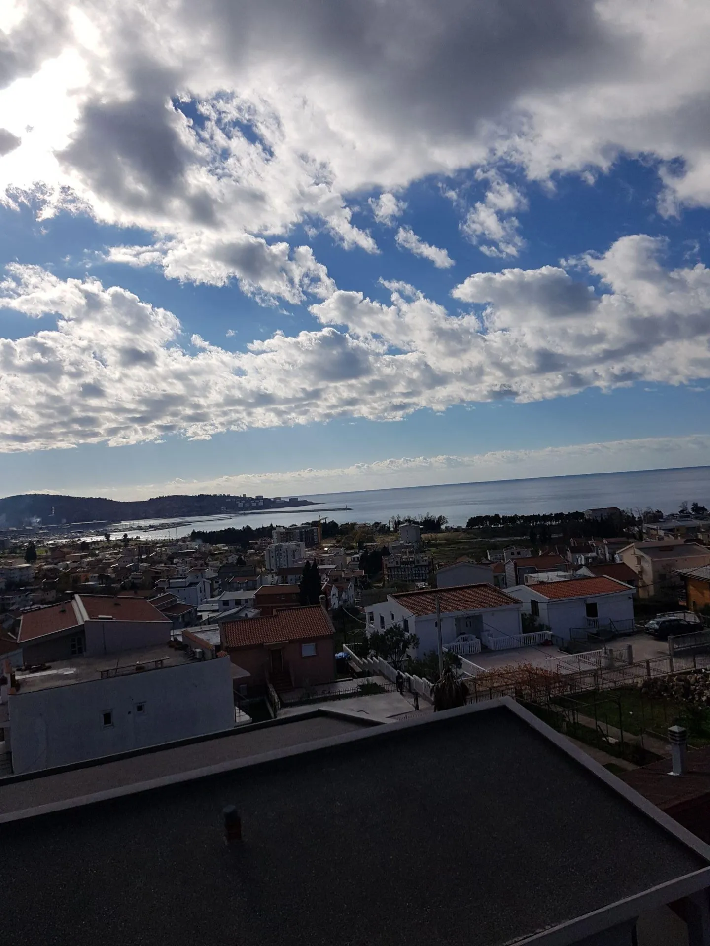 Panoramablick auf das Meer und die Stadt Šušanj in Montenegro vom Dach des Hauses, mit sichtbaren Ziegeldächern und Küstenlandschaft.