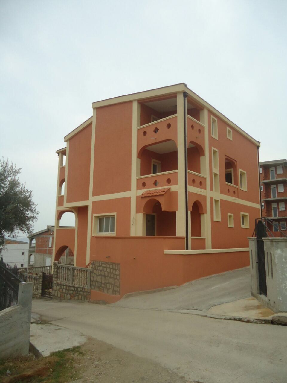 Dreistöckiges terrakottafarbenes Haus mit Bogenbalkonen in Šušanj, Montenegro, Außenansicht.