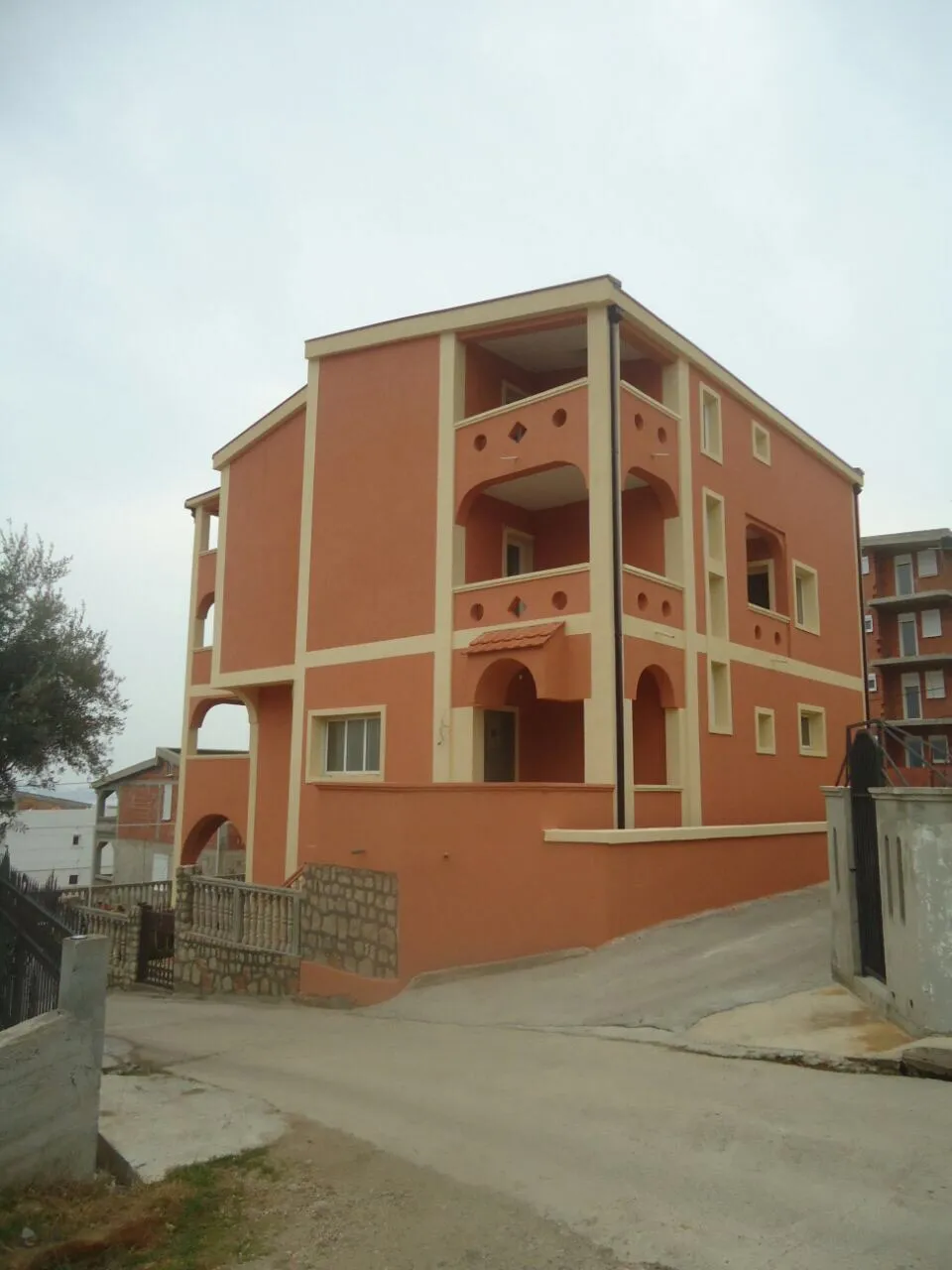 Dreistöckiges terrakottafarbenes Haus mit Bogenbalkonen in Šušanj, Montenegro, Außenansicht.