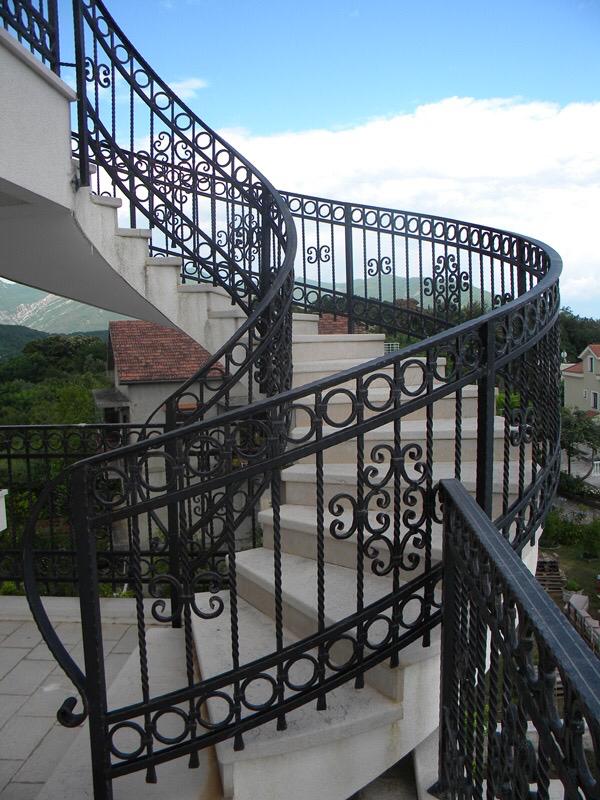 A spiral staircase with wrought-iron railings in a villa in Herceg Novi, Montenegro, with panoramic views of the mountains and the city.