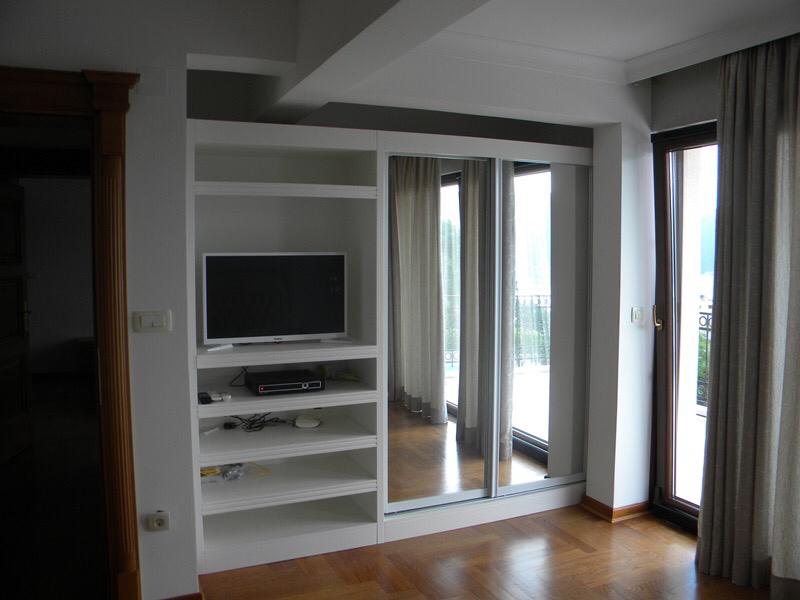 Bedroom interior in a villa in Herceg Novi, Montenegro: white TV shelving unit, mirrored sliding wardrobe, and access to the terrace.