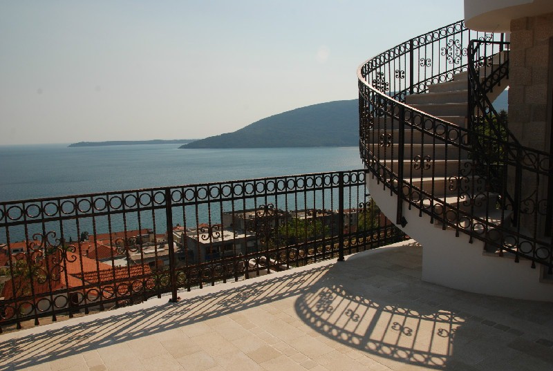Villa terrace in Herceg Novi, Montenegro: wrought-iron spiral staircase, stone floor, and panoramic view of the Adriatic Sea.